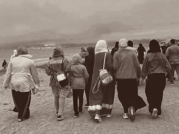 A group of women and children walking together along a beach, seen from behind.